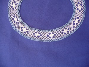 Oval shaped Torchon lace edging in whit with a blue edge. 