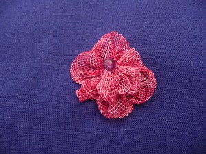A small lace flower made of variegated pink thread with a round dark pink bead in the centre.