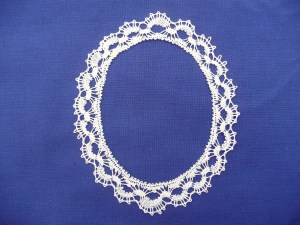 White oval lace edging with whole stitch and spiders on a blue background. 