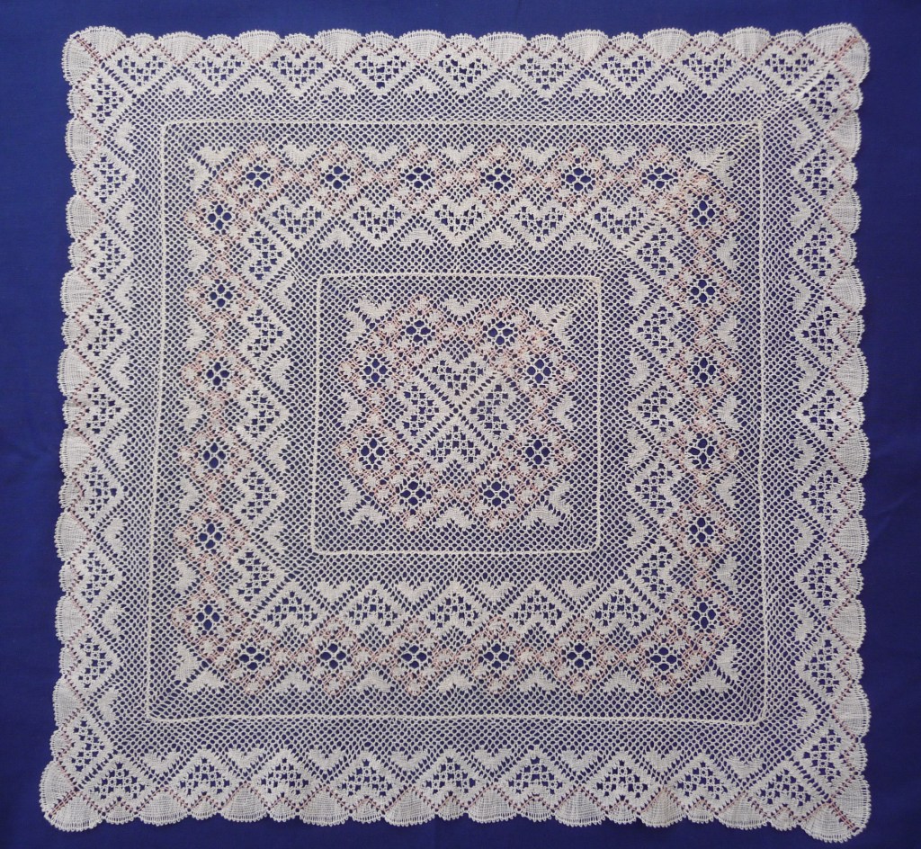 A square lace mat made of white thread with pink highlights, from the designer Bridget Cook - the Hearts and Flowers mat