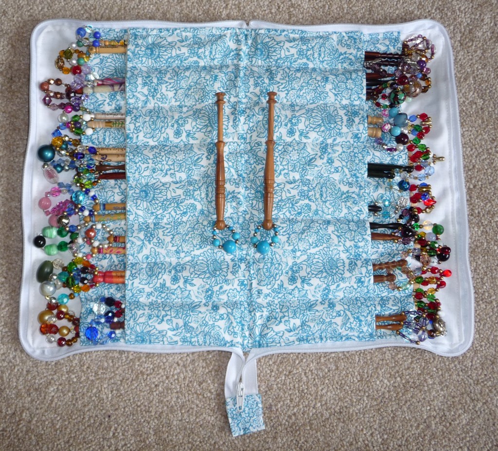 A blue and white fabric bobbin case filled with brightly coloured spangled lace bobbins