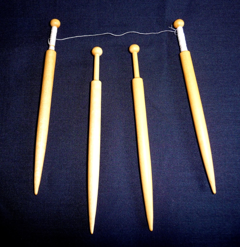 Four light wood Honiton lace bobbins which are tapered at the end. One pair is threaded with white thread.