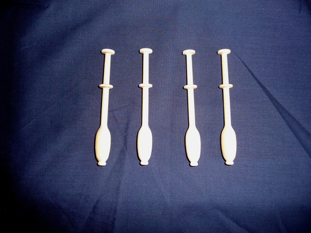 Four wooden continental lace bobbins on a dark blue fabric background