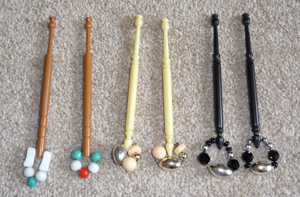 Six plastic lace bobbins- two brown, two cream and two black- with beaded spangles