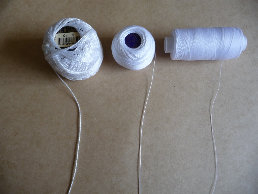 Three spools of white thread of varying thicknesses