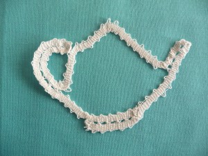 The outline of a teapot made in white tape lace. 