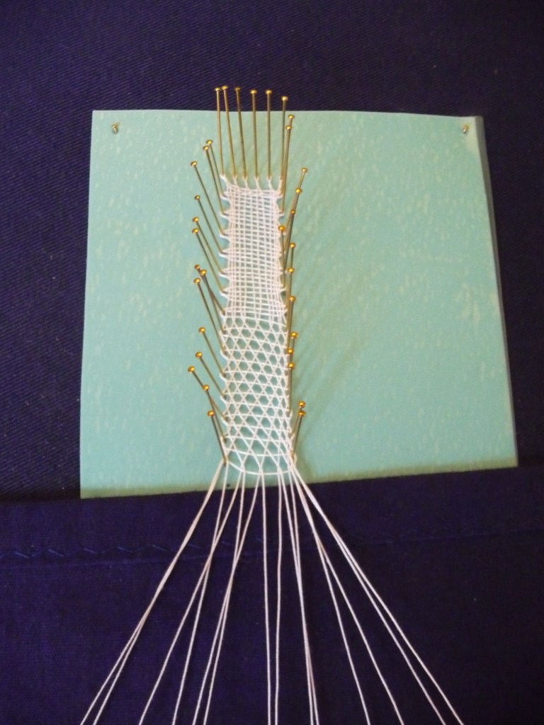 A navy blue lace cushion set up with a strip of whole stitch and half stitch in white thread pinned in the centre