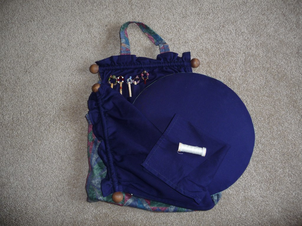 A small round lacemaking travel pillow with a matching bag with spaces for bobbins and a cover cloth